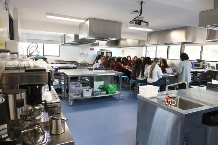 Students seated at a centre table in the middle of a stainless steel industrial kitchen