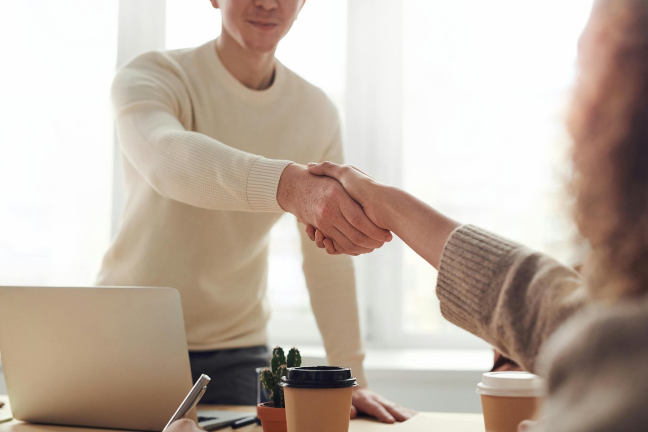 Person in a white jumper standing shaking hands with a seated person.