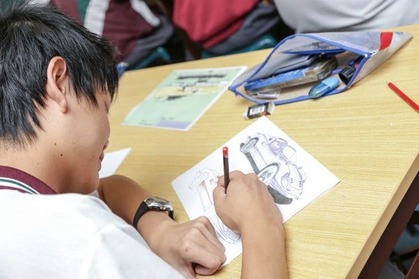 Male student adding shading to a technical drawing of a car