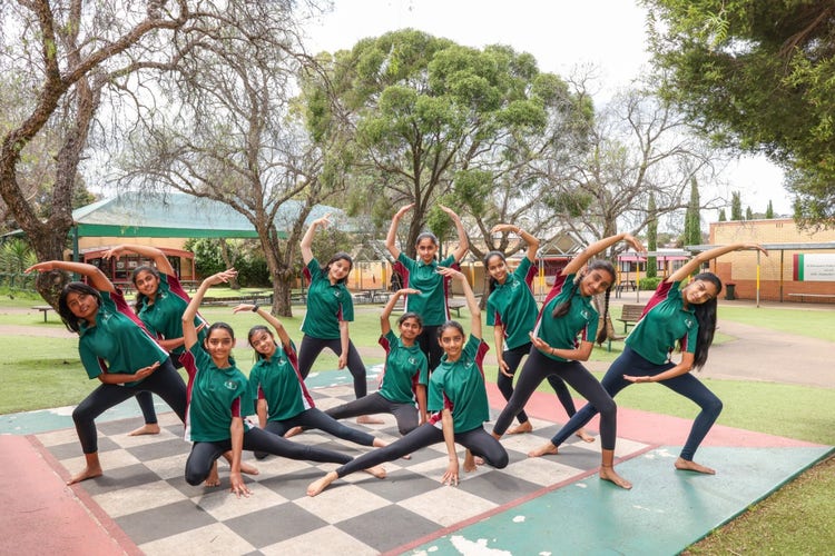 multiple female students in a stretching pose standing on a giant chessboard