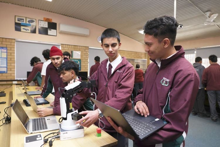 Students programing a robotic arm using a laptop in the classroom