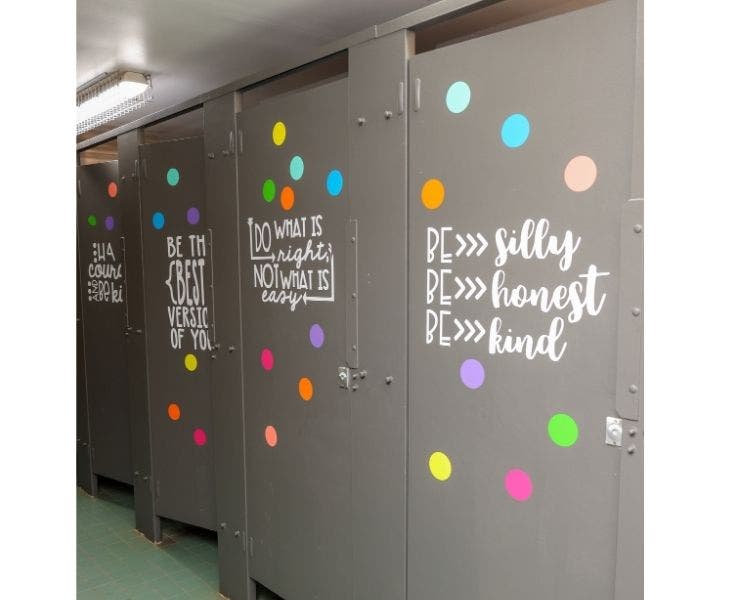 Toilet stall doors repainted grey with multicoloured circles and uplifting quotes